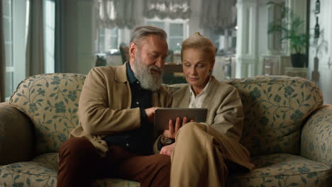 una encantadora pareja madura navegando por internet en un dispositivo digital en una casa de lujo