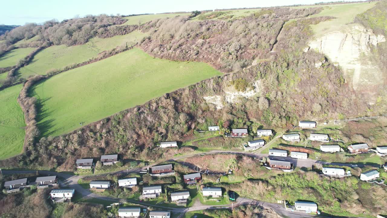 Aerial view of Branscombe village, showing holiday homes nestled on a hillside, with the dramatic cliffs of the Jurassic Coast in the background