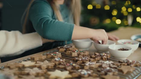 tracking video of caucasian mother and daughter decorating gingerbread cookies with chocolate and sprinkles.