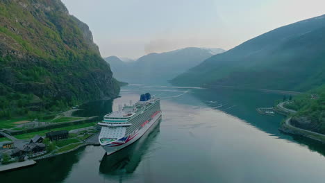 cruise ship sailing through a narrow fjord with towering mountains, calm waters reflecting the serene landscape, aerial view