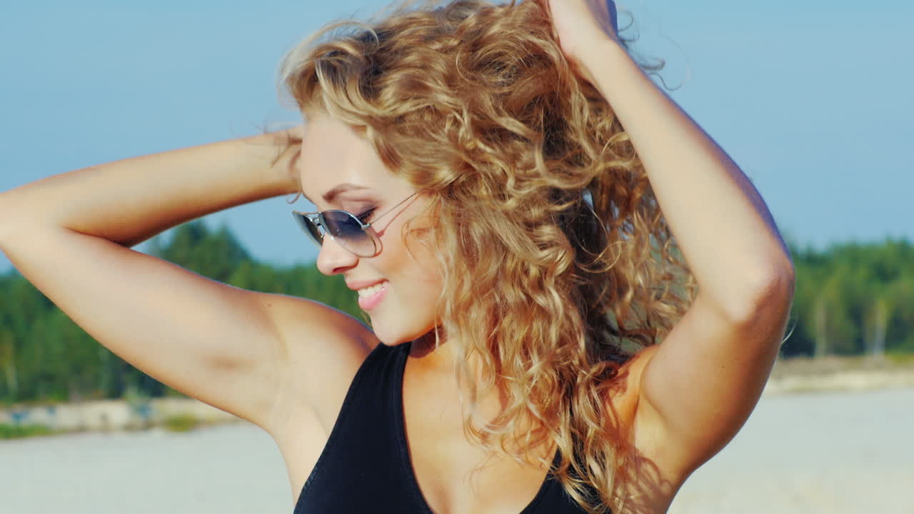 Een aantrekkelijke jonge vrouw met zonnebril poseert glimlachend voor de camera op het strand.