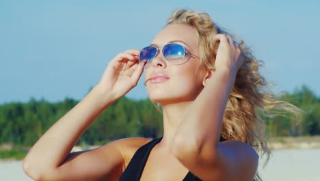 An-Attractive-Young-Woman-In-Sunglasses-Posing-At-The-Camera-At-The-Beach-Smiling
