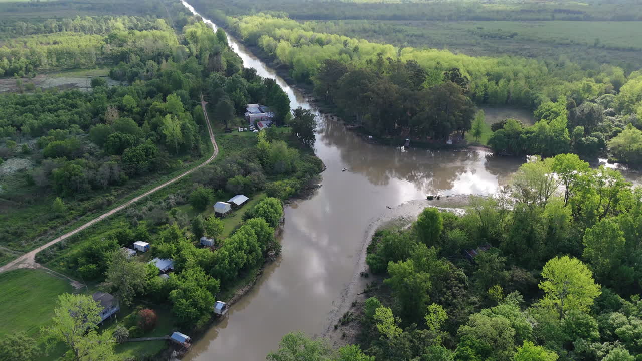Aerial flyover of school and cabins near forest and river in Argentine Delta, rural countryside establishing