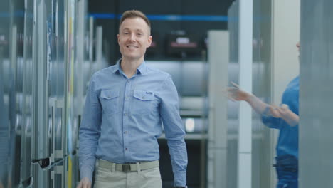 A-young-man-dances-in-an-electronics-store-and-looks-at-the-camera,-a-woman-jumps-out-and-hugs-him-smiling-and-laughing.