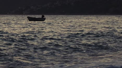 fishing boat anchored near shoreline of mediterranean village, floating on shallow lagoon at dusk, sea waves splashing on bay