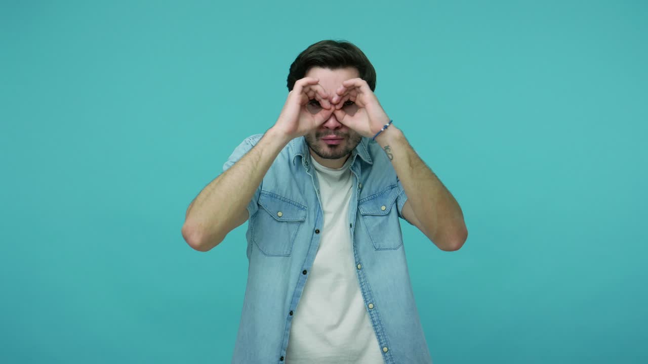 un tipo curioso con una camisa de vaqueros mirando a través de un gesto binocular, buscando algo en la distancia, mirando desde lejos