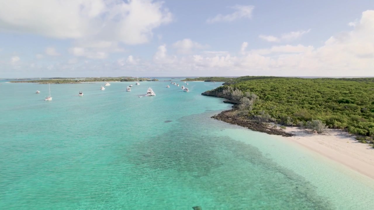Luftfoto fra drone af en ensom båd, der flyder over krystalklart turkisblåt vand og koralformationer på Bahamas.