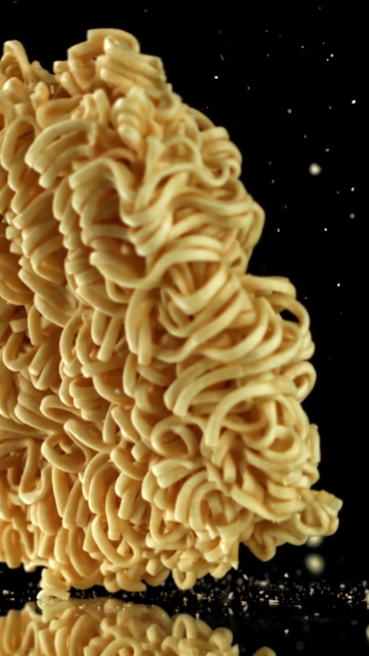 Noodles istantanei secchi che cadono al rallentatore su uno sfondo nero