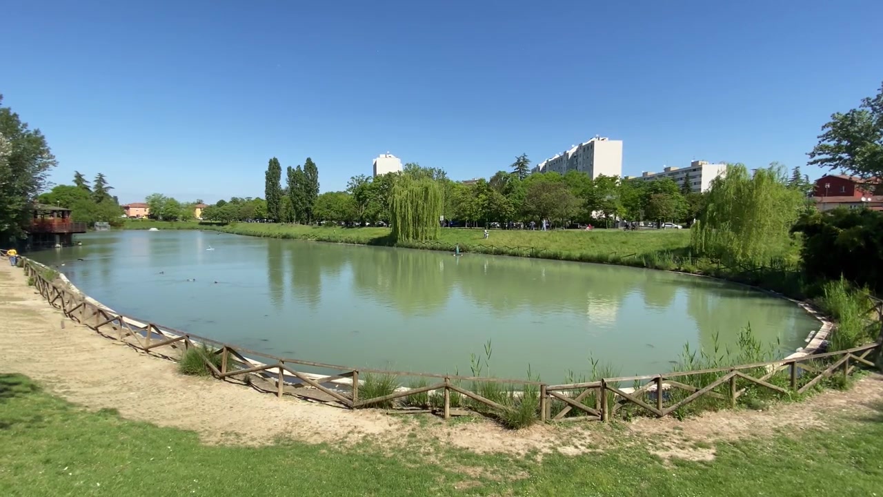 Parco della Ca' Bura à Bologne, Italie. Magnifique lac, oasis urbaine avec poissons et faune, une clôture en bois, de l'herbe verte et des bâtiments résidentiels. 4K.