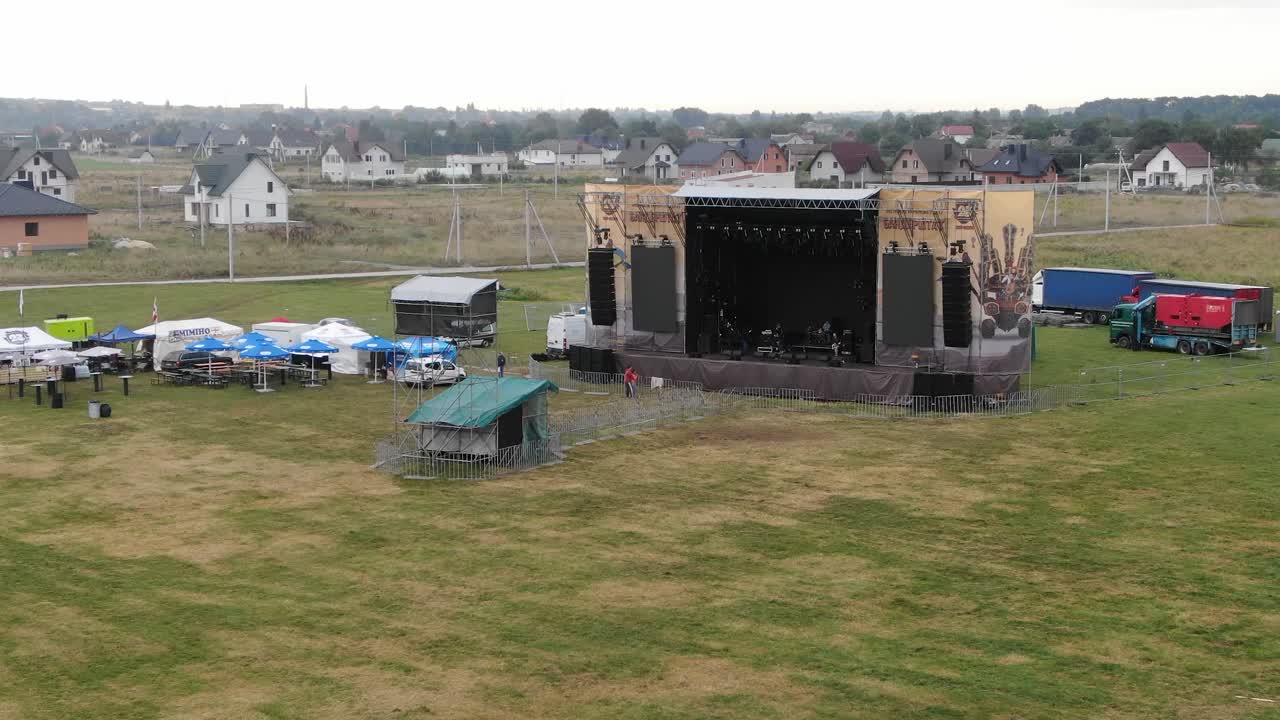 Aerial View of Multi-Colored Tents Pitched in a Field at a Music Festival Tracking Forward Showing Campfire and Stage