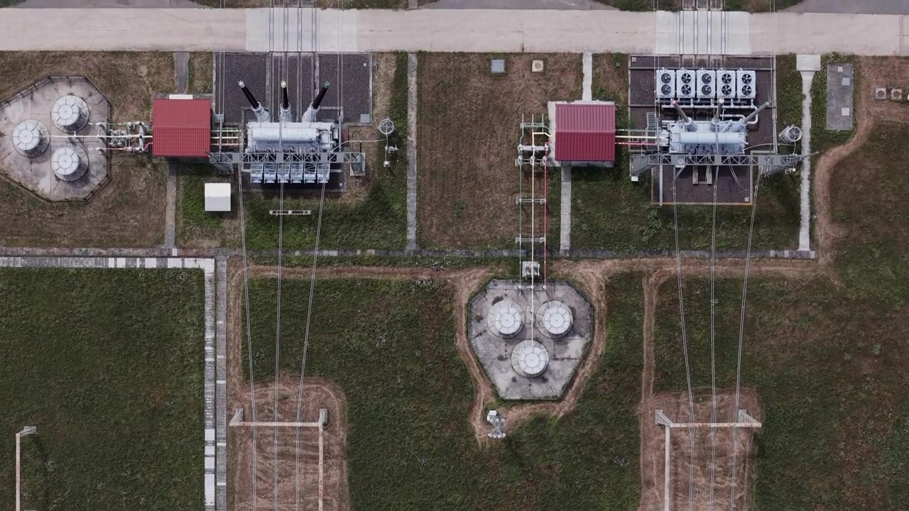 Letecký pohled shora ukazuje elektrickou rozvodnu s přenosovými vedeními rozprostírajícími se přes venkovské pole, zdůrazňující kritickou energetickou infrastrukturu.