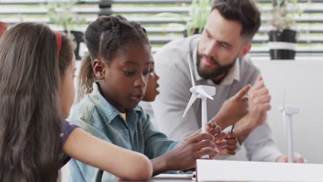 diverse male teacher and happy schoolchildren studying wind turbines in school classroom
