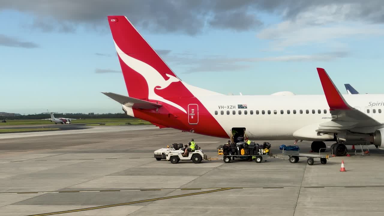 Ground crew services a Qantas aircraft at Brisbane Airport, involving luggage handling and vehicle movement under clear skies
