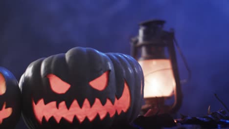 Video-of-halloween-carved-pumpkins,-lantern-and-smoke-with-copy-space-on-purple-background