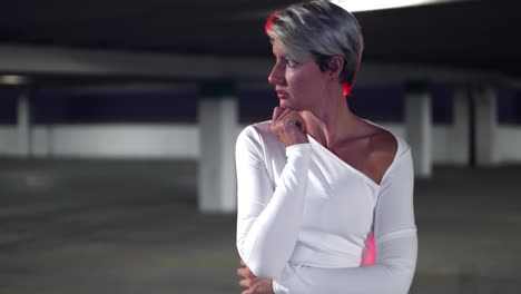 hermosas mujeres rubias blancas caucásicas de pelo corto que actúan nerviosas y asustadas en un estacionamiento subterráneo con vestido blanco y luz roja detrás de ella