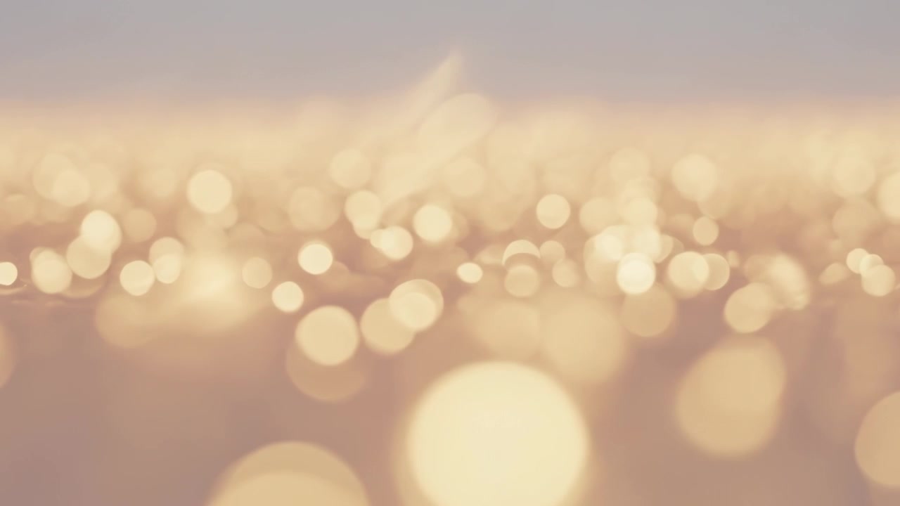 Shimmering broad golden bokeh field shifting across water at sunset, camera focus sliding