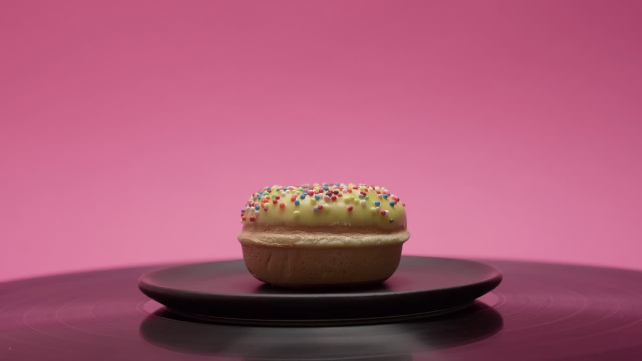 A delicious yellow donut with colorful crumbs rotates on a pink background
