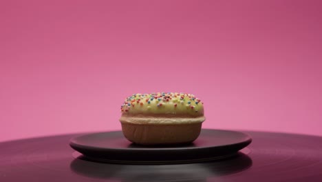 A delicious yellow donut with colorful crumbs rotates on a pink background