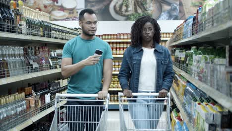 focused young couple walking in aisle with alcohol drinks