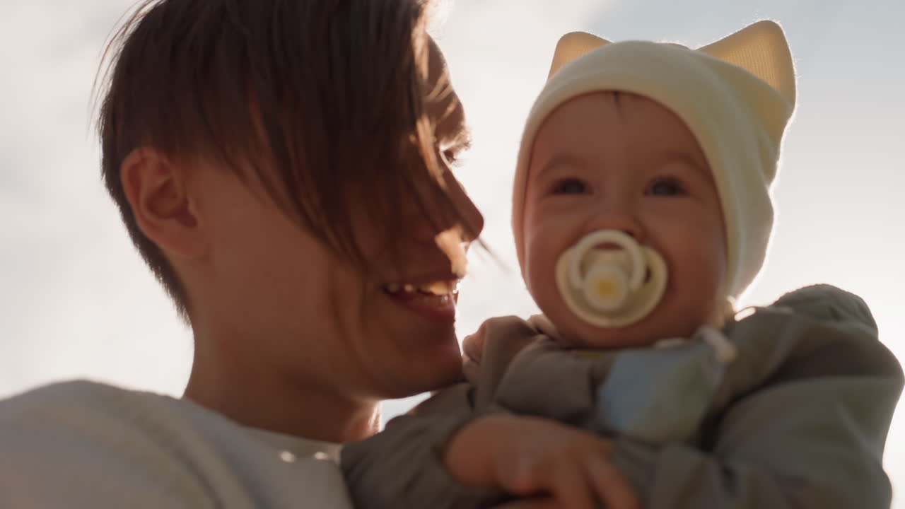 White father smiling with baby sunlight. Warm glow and gentle backlight, pacifier and cute beanie, joyful laughter and proud embrace, candid portrait, affectionate family closeness and playful