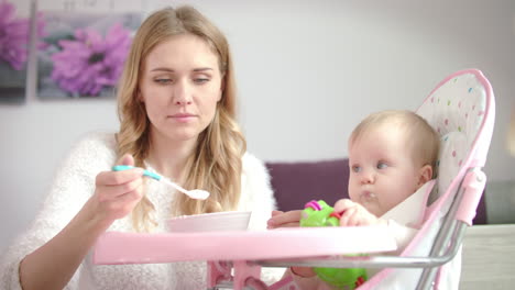 Niño-Con-Juguete-Comiendo-Comida-En-Puré-Del-Tazón-Para-Bebés.-Mujer-Alimentando-Al-Bebé-En-Una-Silla