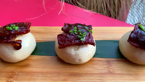 mini bao buns with glazed bacon in bbq sauce and fresh chives, hot asian steamed buns in a restaurant, 4k shot