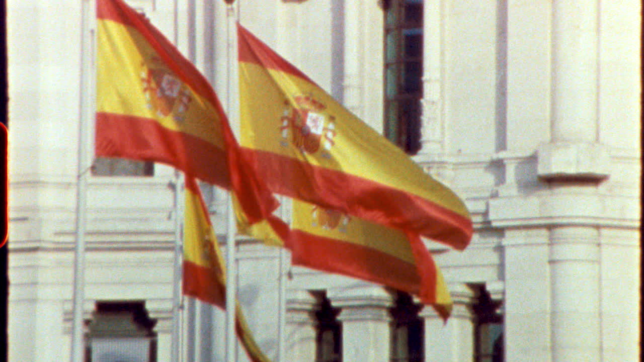 Spanish national flags gently waving, blowing in bright sunlight against white historic building facade in Madrid urban landscape, symbolizing national pride and cultural identity - filmed on vintage super 8 camera