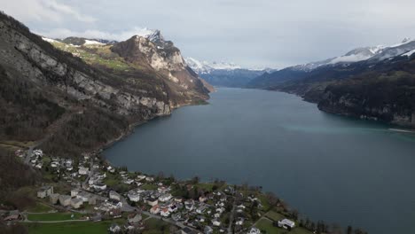 Vista-Aérea-Panorámica-De-La-Comunidad-En-La-Costa-Del-Lago-Walen-En-Walensee,-Suiza,-En-Un-Día-Nublado