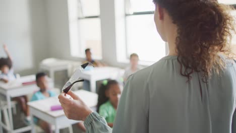 Video-of-back-view-of-caucasian-female-teacher-conducting-lesson-in-class-of-diverse-pupils