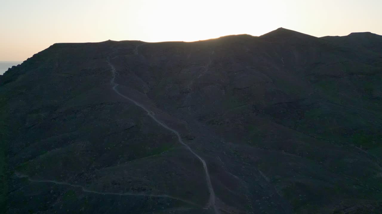 toma aérea siguiendo el sendero hasta la cima de una montaña, revelando la hermosa puesta de sol