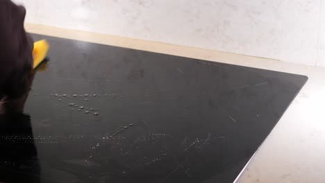 woman cleaning a black stovetop in a kitchen