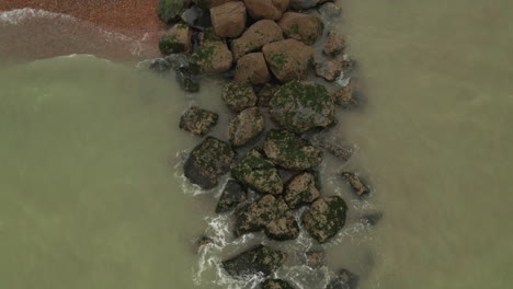 aerial top down view of breakwater hitting rocks on the coastline, on the south coast of england, starting close and rising up