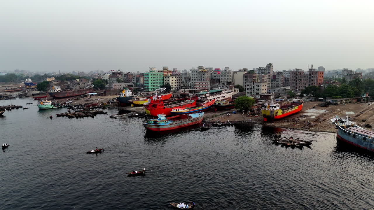 Aerial drone shot flying over the Buriganga river toward docked cargo ships in Dhaka, Bangladesh.