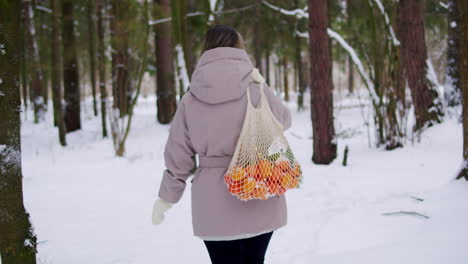 woman in winter forest carrying oranges in a string bag