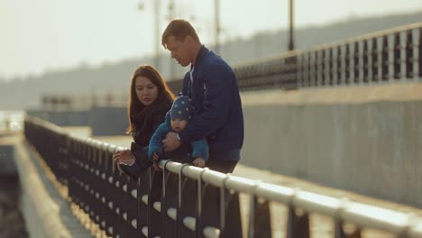 los padres hablan en el muelle en el parapeto, el bebé está sentado. infancia feliz en una familia internacional. movimiento circular de la cámara.
