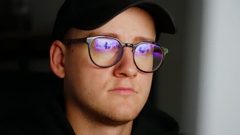 man working indoors at a computer, computer screen reflecting from his glasses