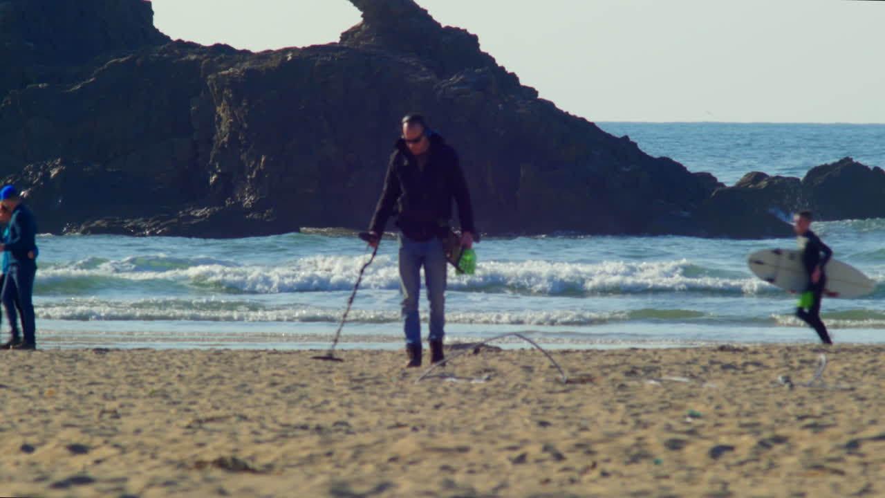 Man waves metal detector on beach with ocean in background