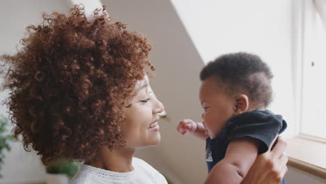 mother playing game with newborn baby son and lifting him in air in loft apartment