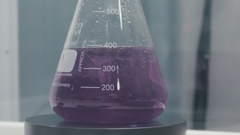 stirring test tubes containing purple chemical liquids while working in a modern laboratory