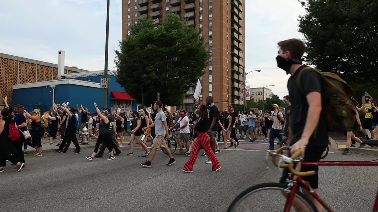 Slow motion view of people marching and blocking traffic as they protest against deaths of unarmed black men at hands of police. Black Lives Matter movement and gathering in the city.