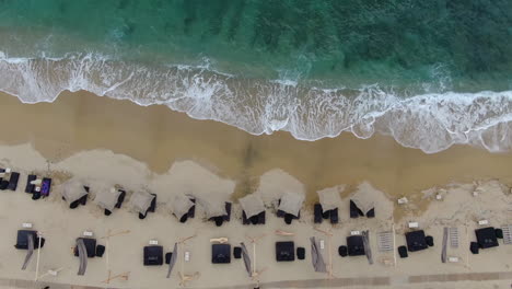waves of azure ocean crashing in over golden sand beach lined with sunbeds