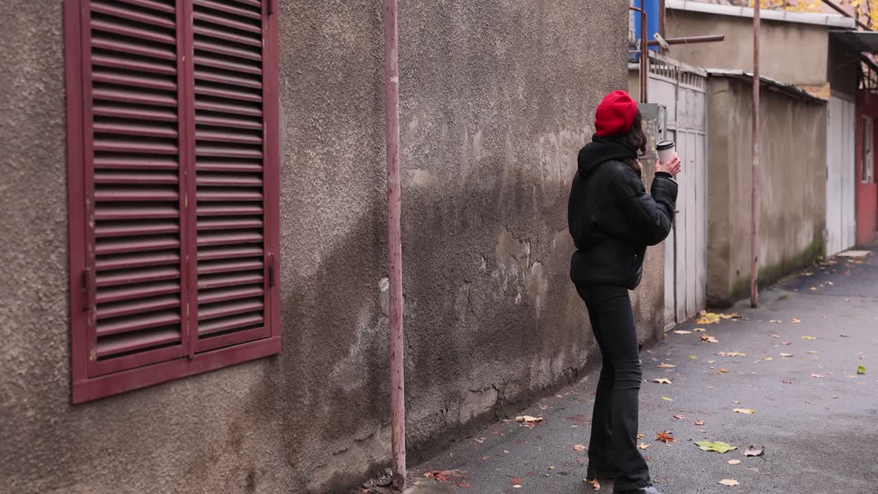Woman in red beret and black jacket walking down the street with coffee