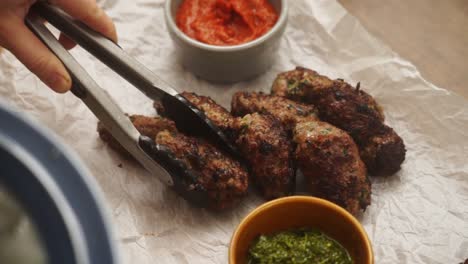 faceless cook putting appetizing fried meat pieces on parchment with bowl of sauce