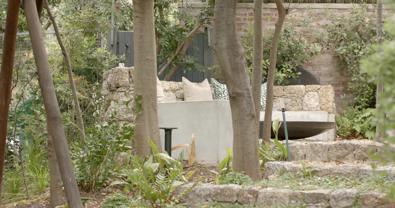 La telecamera sta panoramando per rivelare un angolo salotto in pietra integrato con cuscini in un giardino terrazzato.