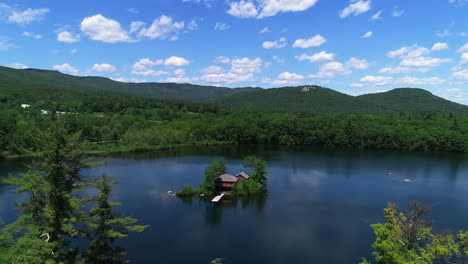 Drone-footage-of-serene-NH-White-Mountains-lake,-isolated-island-house,-and-natural-beauty