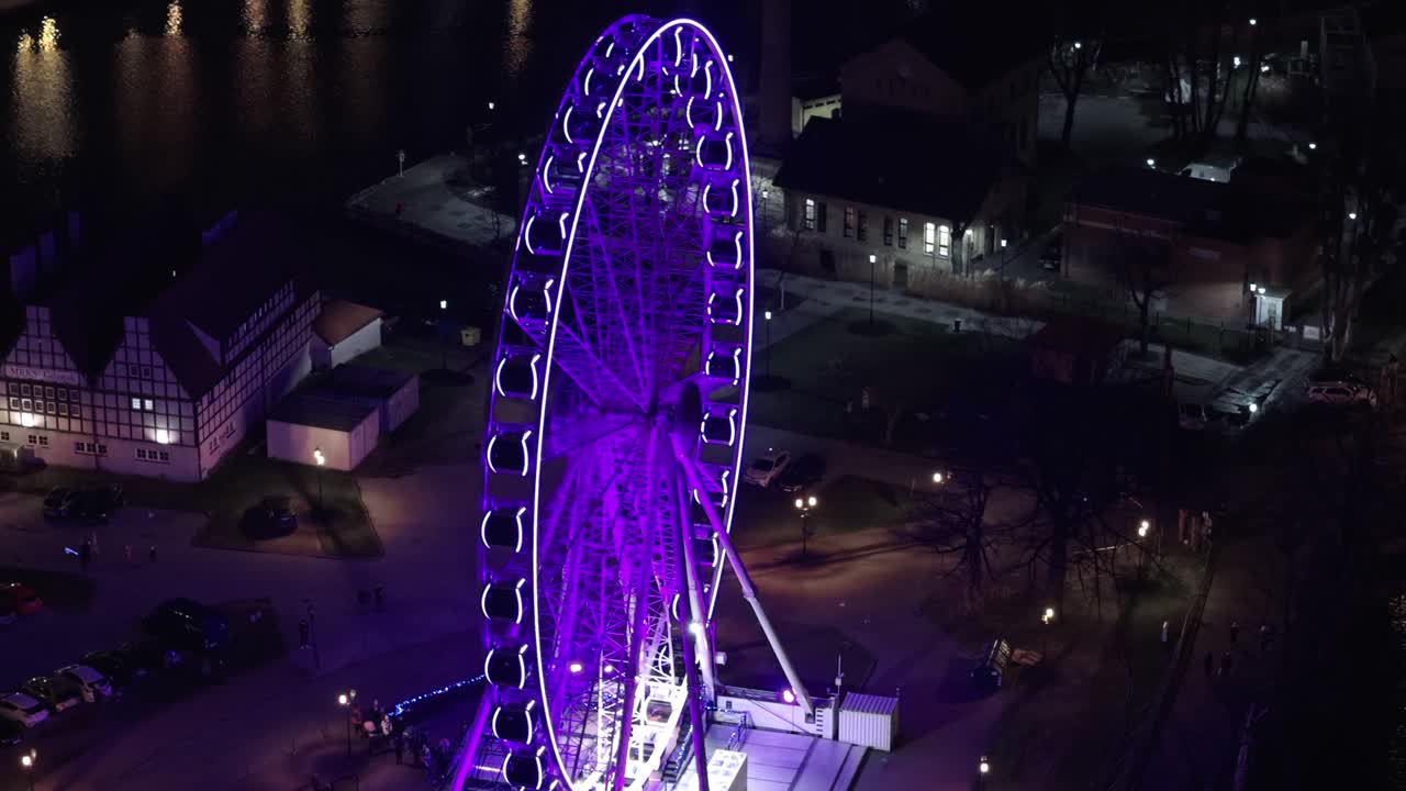 Aerial orbit shot of lighting Ferris wheel named amber skye in Gdańsk city at night. Lighting lantern of historic buildings and motlawa river in background. Poland, Europe