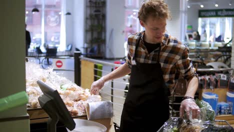 caucasian young worker arranging potatos at grocery shop. guy in apron weigh paacks of healthy organic potatos in supermarket on electronic scales, puts stickers with price