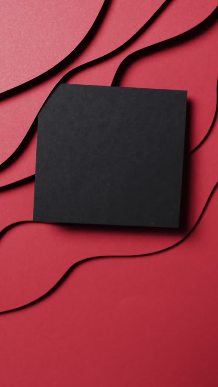 Vertical video of square of black paper on waves cut out and copy space on red background