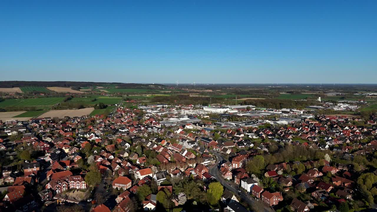 Aerial backwards shot of american town with countryside fields and wind turbines in distance. Sunny day with blue sky in spring Panorama view.