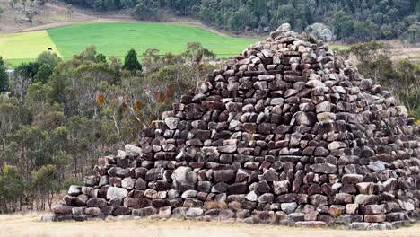a large stone pyramid stands in a dry, rural landscape near stanthorpe, australia. the camera slowly pans, revealing surrounding bushland under natural daylight